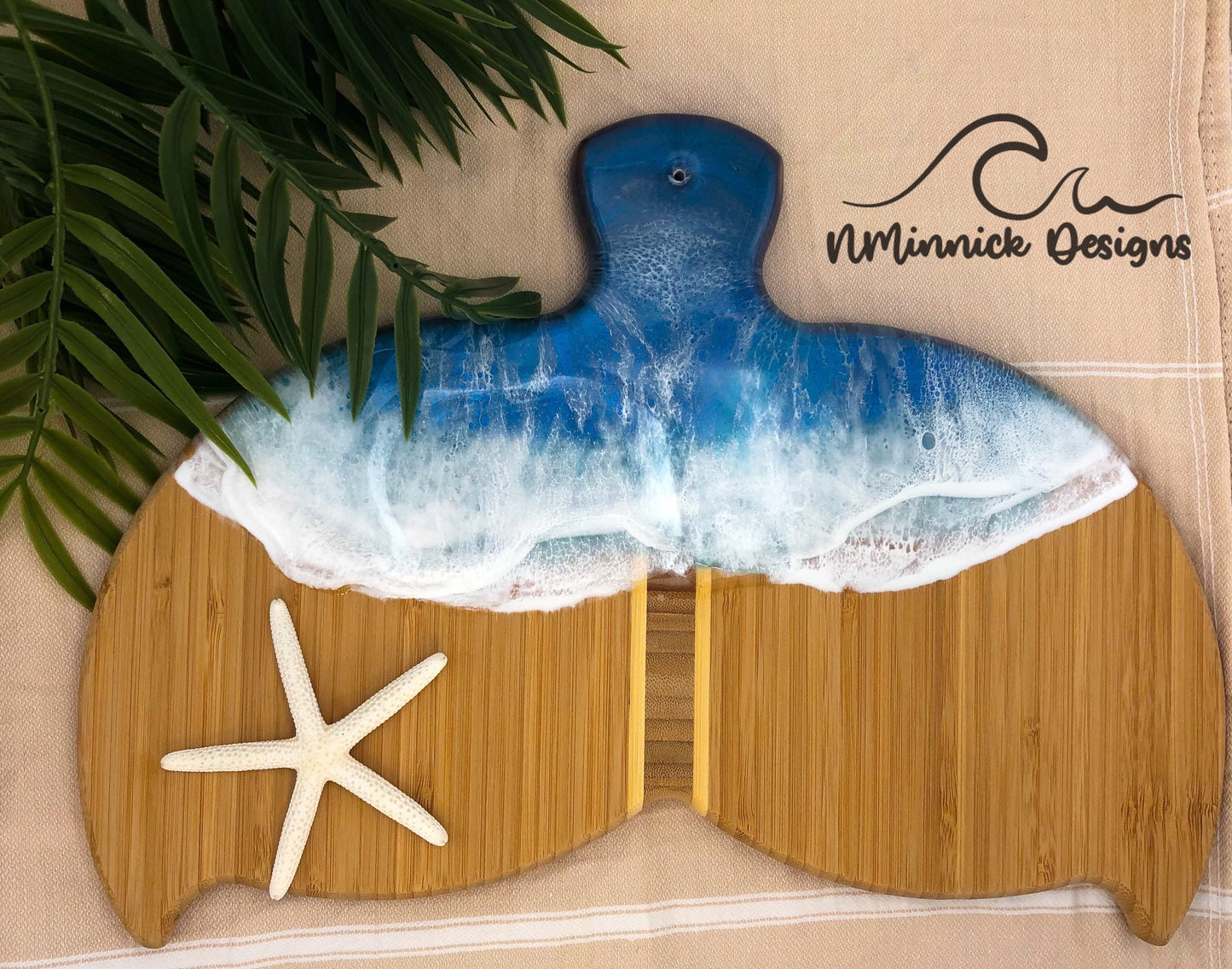 14.5 inch x 10.5 inch bamboo serving board in the shape of a whale fin with a dark navy blue and medium blue ocean wave pattern on the top half of the board.