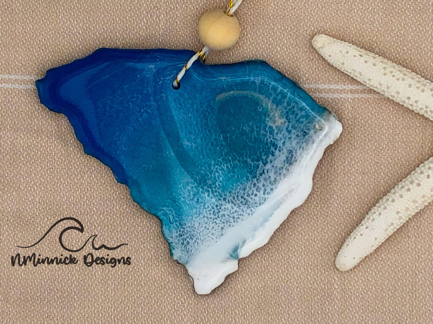 South Carolina shaped wood ornament, appox 4 inches, with blue and teal ocean and white ocean wave pattern and finished with gold and white twine and wooden beads.