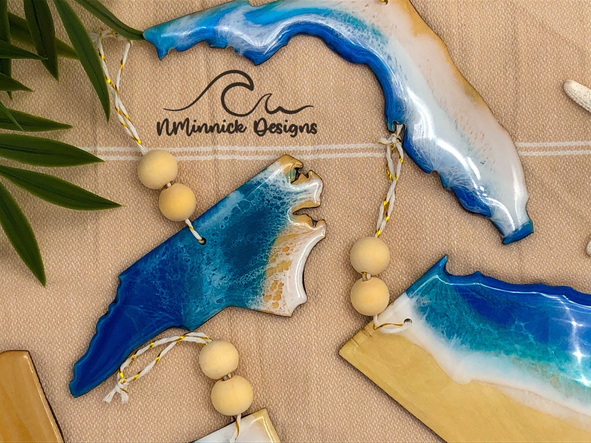 North Carolina-shaped wooden Christmas ornament covered in blue and teal colored ocean resin art resembling the waves along North Carolina&#39;s Atlantic Coast. Finished with blue and white baker&#39;s twine and two wooden beads.