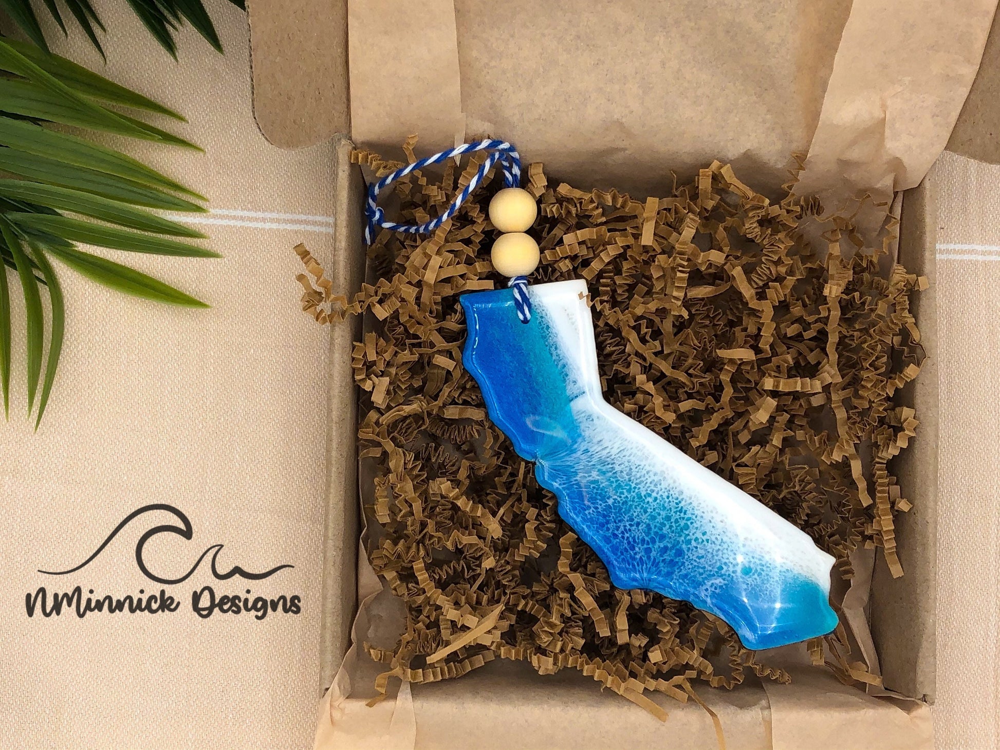 4 to 4.5 inch california shaped ocean resin ornament in dark blue and okinawa blue for a one of a kind ocean wave pattern. Finished with bakers twine and two wooden beads and packaged in ecofriendly plastic free materials.