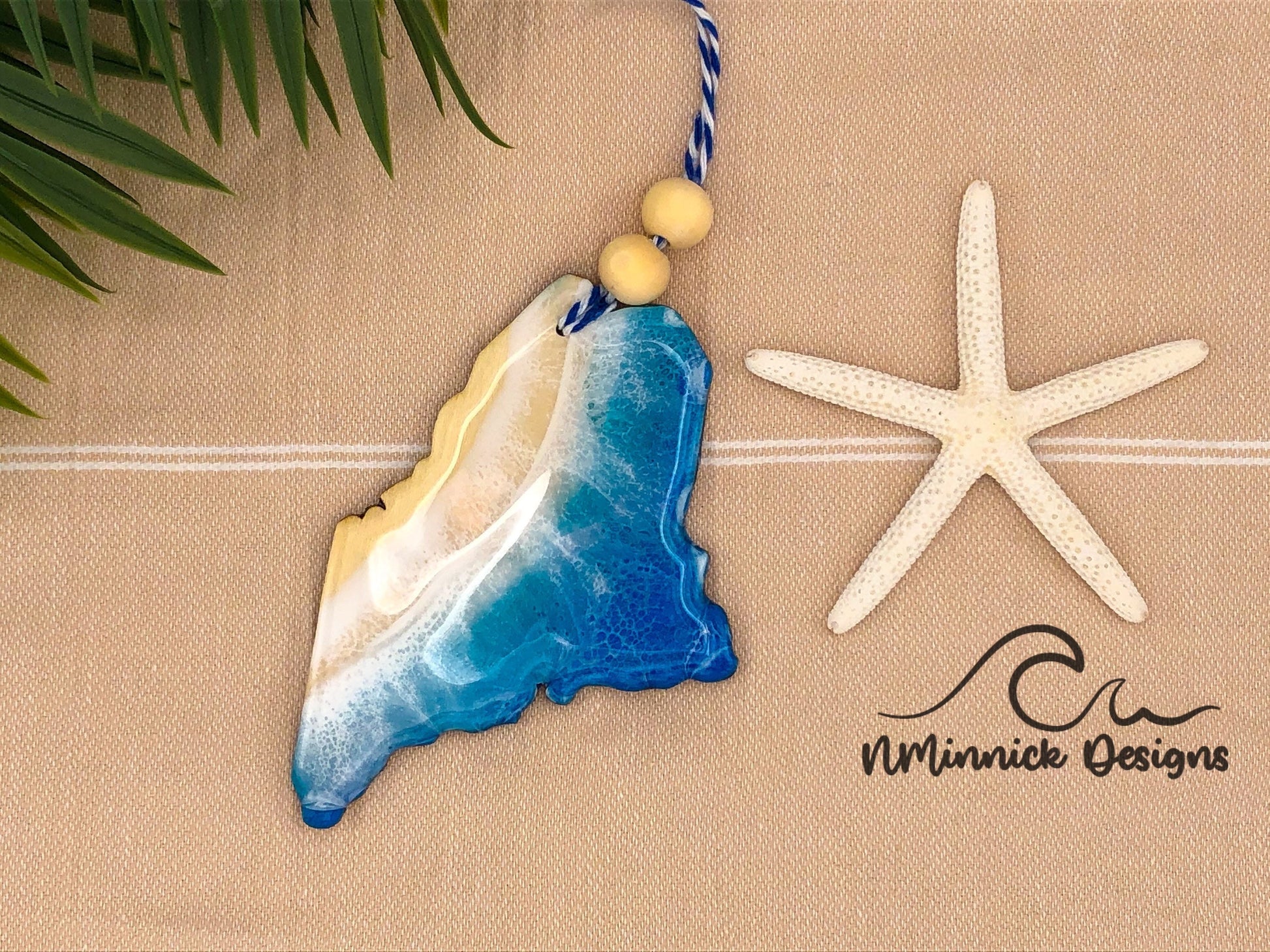 Maine-shaped wooden Christmas ornament covered in blue and teal colored ocean resin art resembling the waves along Maine&#39;s Atlantic Coast. Finished with blue and white baker&#39;s twine and two wooden beads.