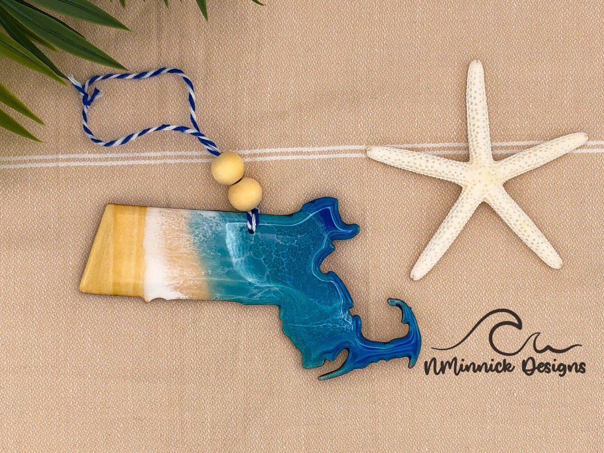 Massachusetts ocean resin ornament, dark blue and teal with white ocean waves made with epoxy resin. Finished with bakers twine and two wooden beads.