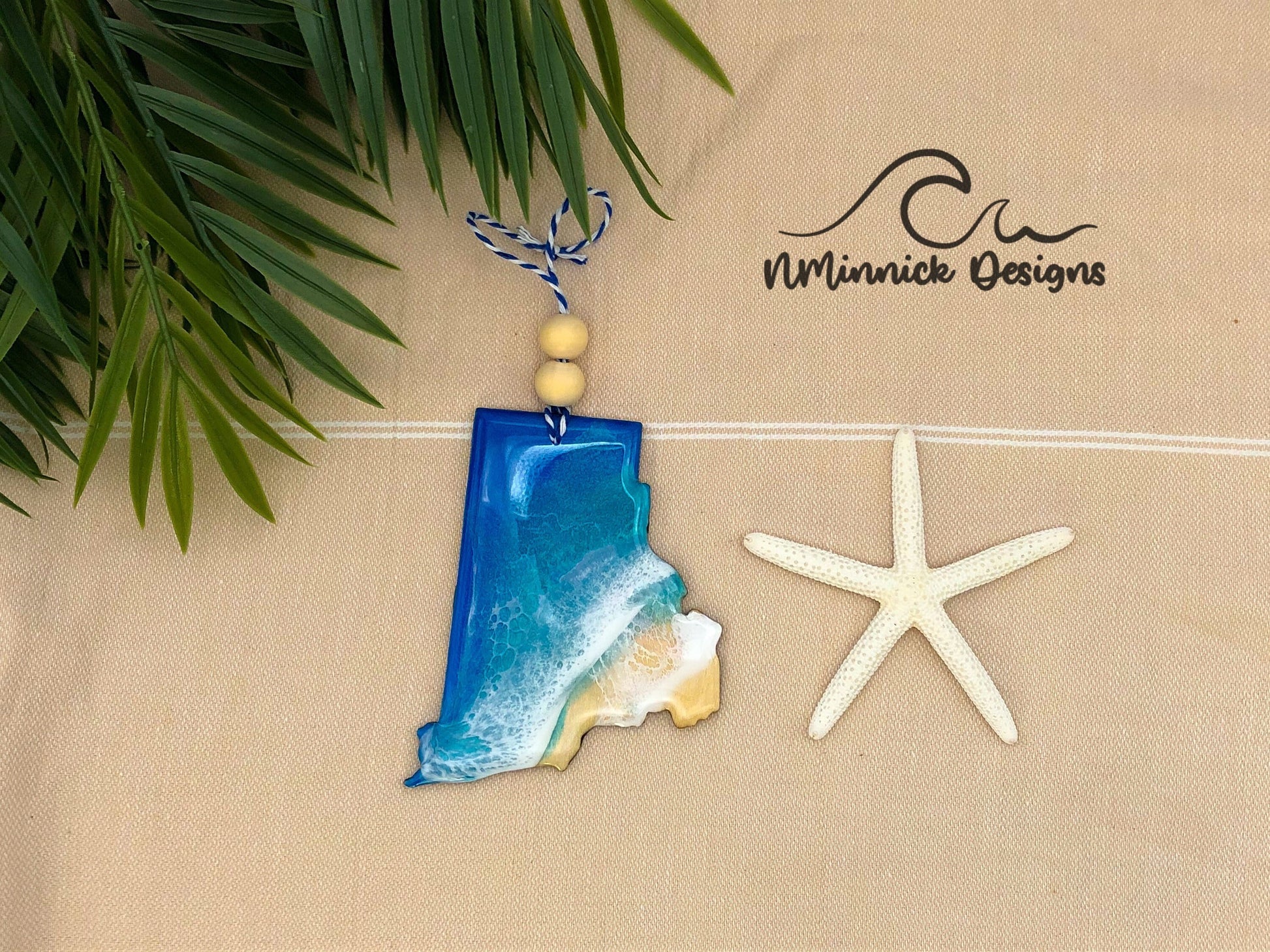a laser cut wood ornament in the shape of Rhode Island. Ornament is approx 4 inches long and 1/8 inch thick and is covered in blue, teal, and white epoxy to make it look like ocean waves on a beach.