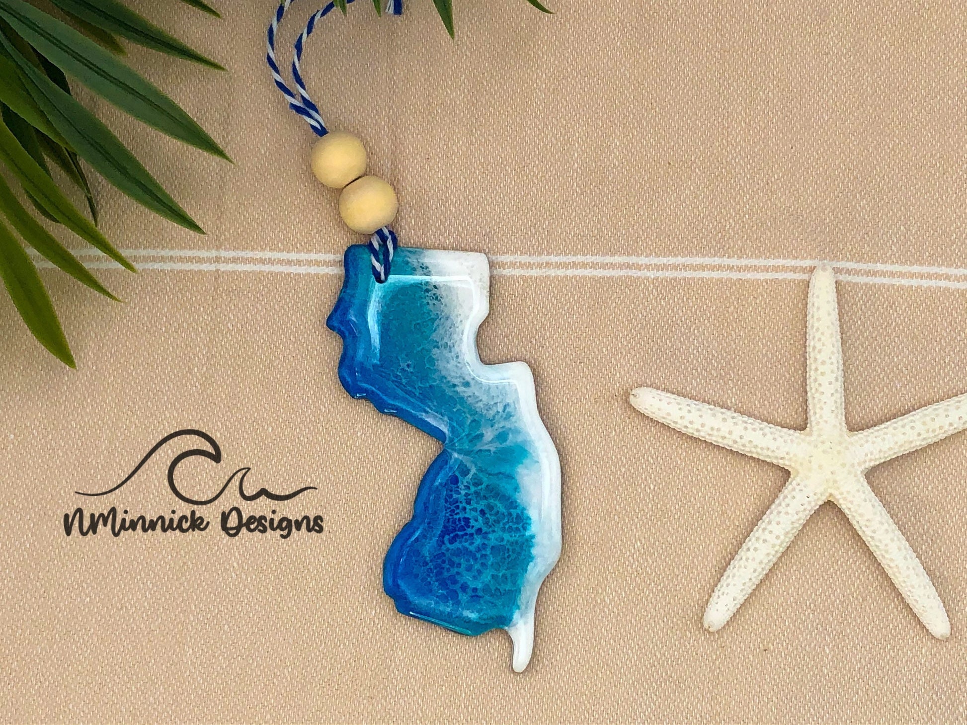 New Jersey-shaped wooden Christmas ornament covered in blue and teal colored ocean resin art resembling the waves along New Jersey&#39;s Atlantic Coast. Finished with blue and white baker&#39;s twine and two wooden beads.