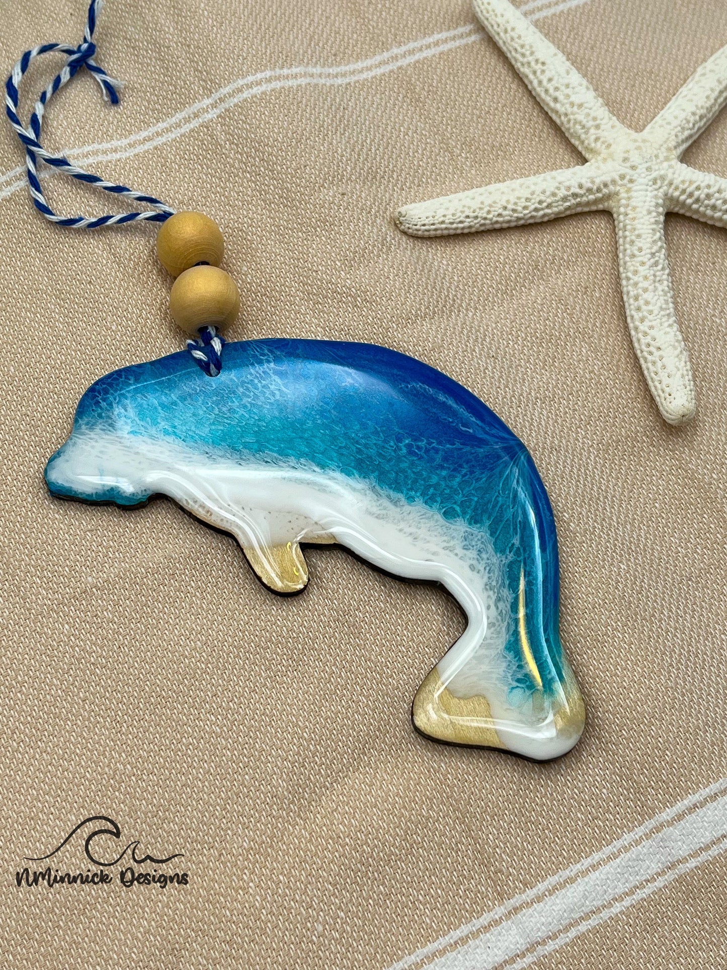Manatee-shaped wooden Christmas ornament covered in blue and teal ocean resin art resembling the waves of the ocean. Finished with blue and white baker&#39;s twine and two wooden beads.