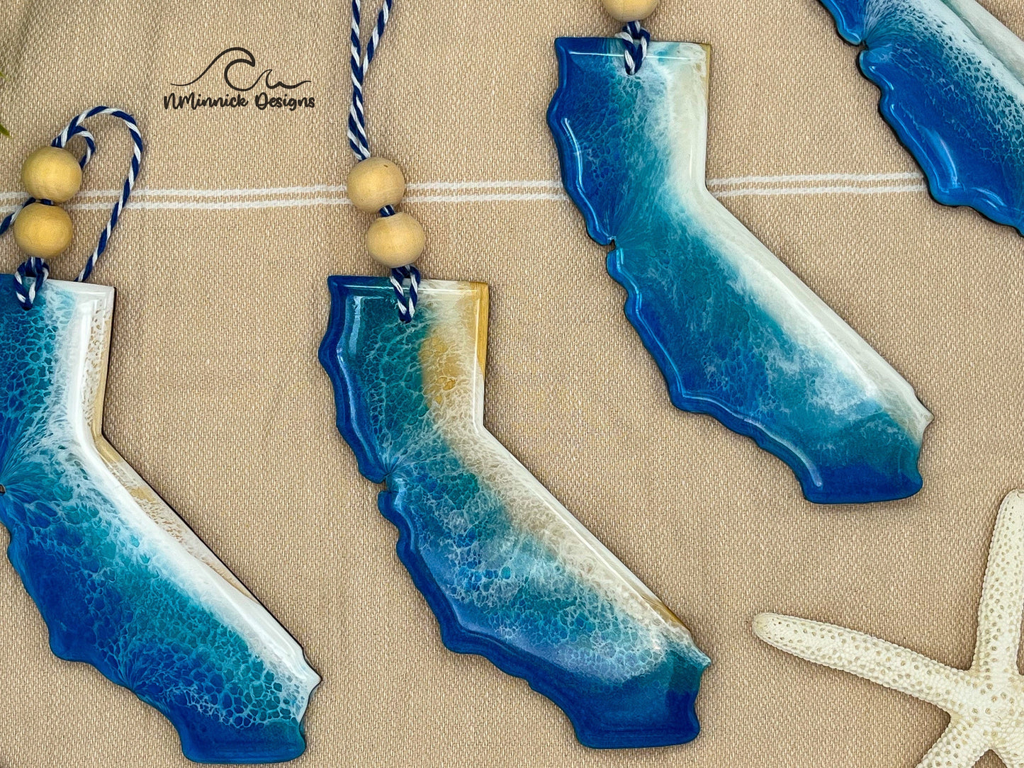 California-shaped wooden Christmas ornament covered in blue and teal colored ocean resin art resembling the waves along California&#39;s Pacific Coast. Finished with blue and white baker&#39;s twine and two wooden beads.