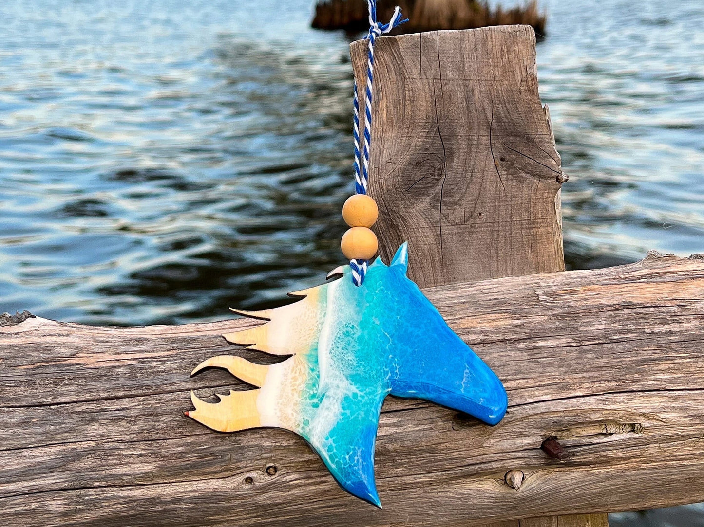 Wood Christmas ornament in the shape of a Horse head with flowing mane. Decorated with blue and teal ocean resin art resembling the waves along the Outer Banks of North Carolina. Finished with blue and white bakers twine and two wooden beads.