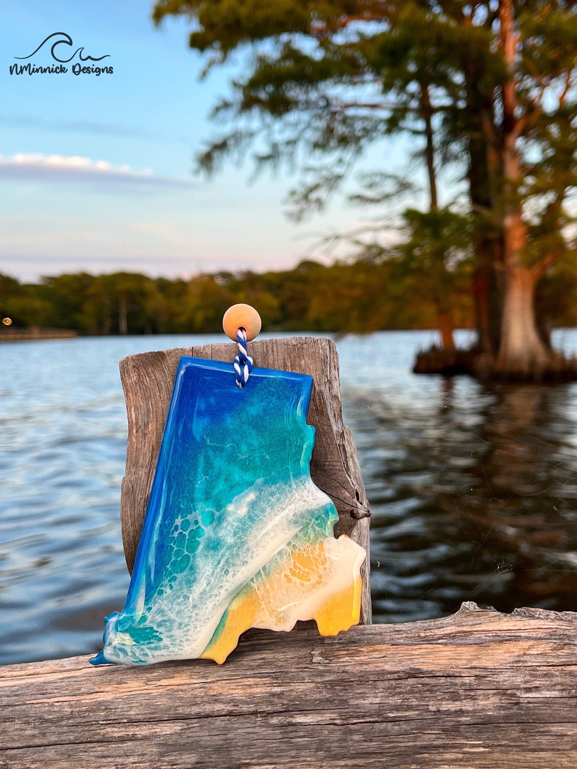 Rhode Island-shaped wooden Christmas ornament covered in blue and teal colored ocean resin art resembling the waves along Rhode Island&#39;s Atlantic Coast. Finished with blue and white baker&#39;s twine and two wooden beads.