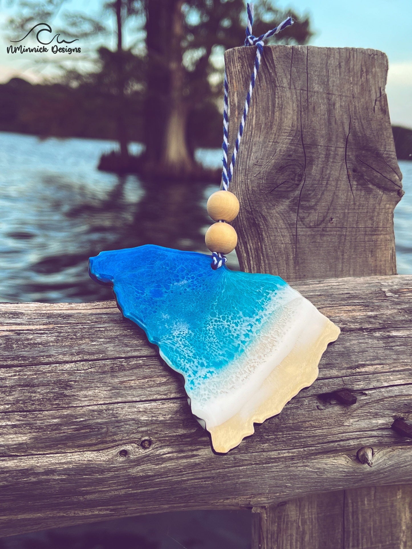 South Carolina-shaped wooden Christmas ornament covered in blue and teal colored ocean resin art resembling the waves along South Carolina&#39;s Atlantic Coast. Finished with blue and white baker&#39;s twine and two wooden beads.