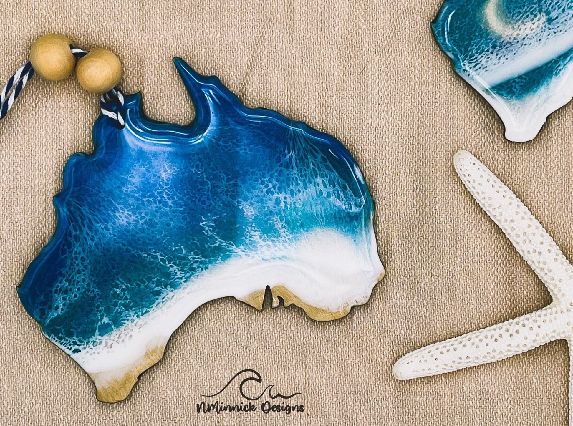 Australia-shaped wooden Christmas ornament covered in blue and teal ocean resin art resembling the waves of the Sunshine Coast. Finished with blue and white baker&#39;s twine and two wooden beads.