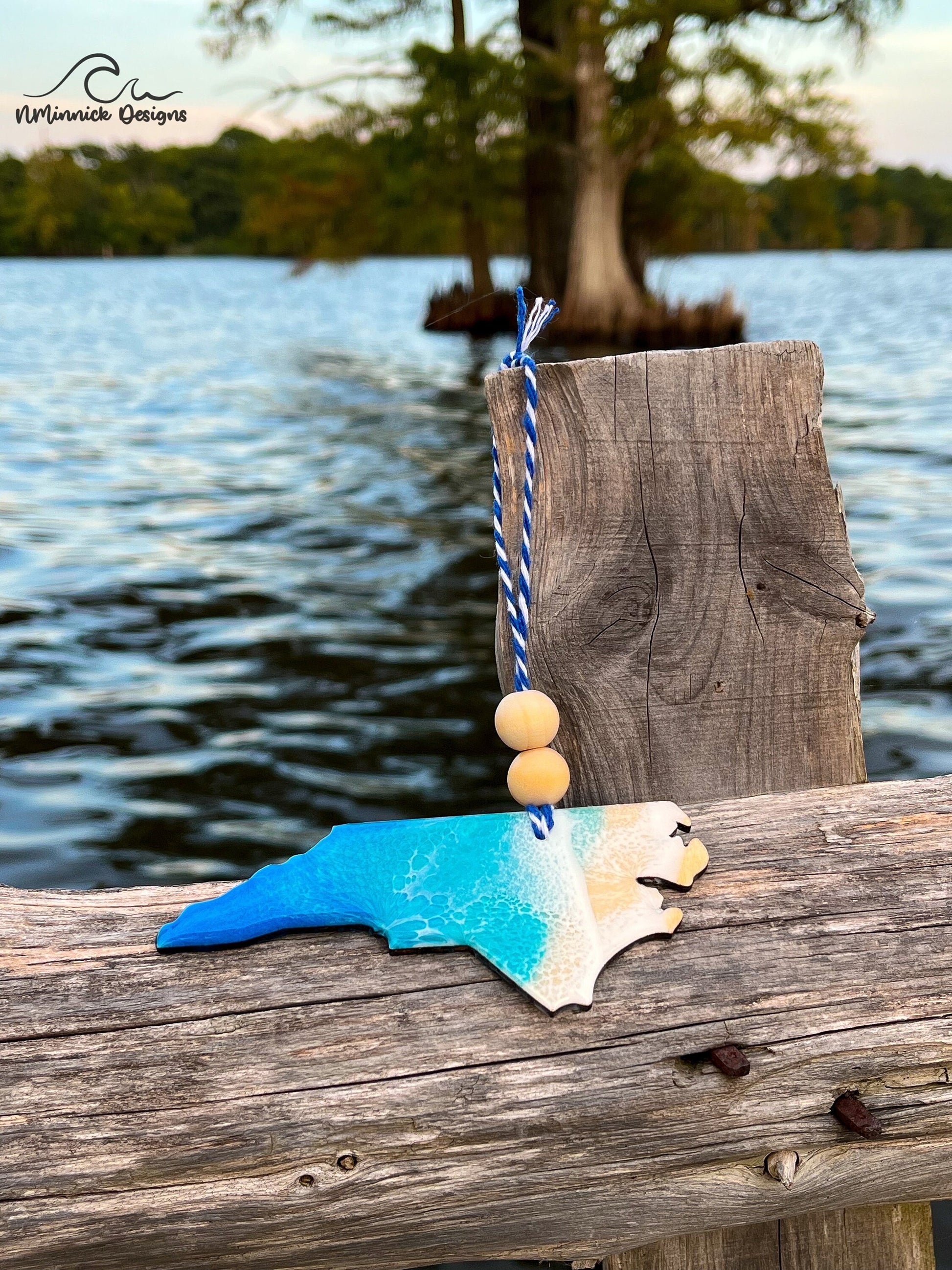 North Carolina-shaped wooden Christmas ornament covered in blue and teal colored ocean resin art resembling the waves along North Carolina&#39;s Atlantic Coast. Finished with blue and white baker&#39;s twine and two wooden beads.