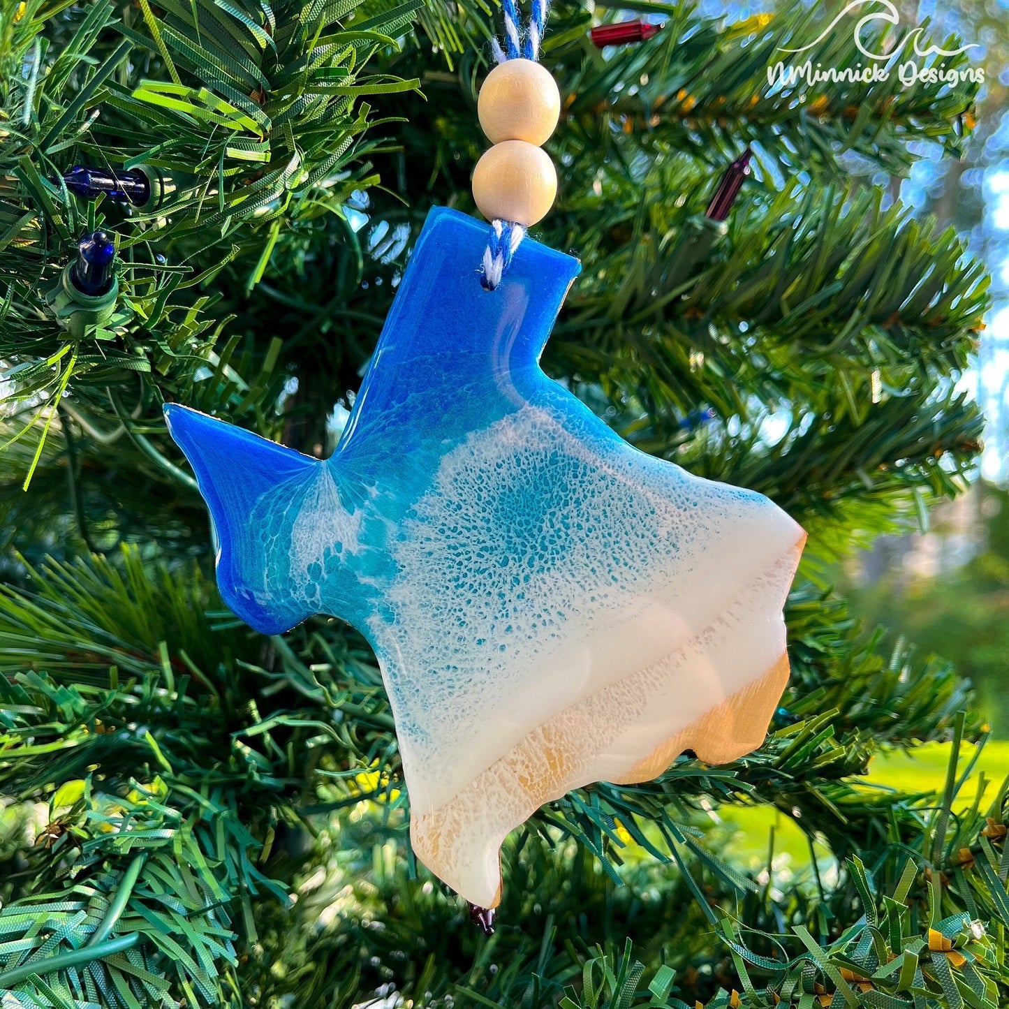 Texas-shaped wooden Christmas ornament covered in blue and teal colored ocean resin art resembling the waves along Texas&#39; Gulf Coast. Finished with blue and white baker&#39;s twine and two wooden beads.