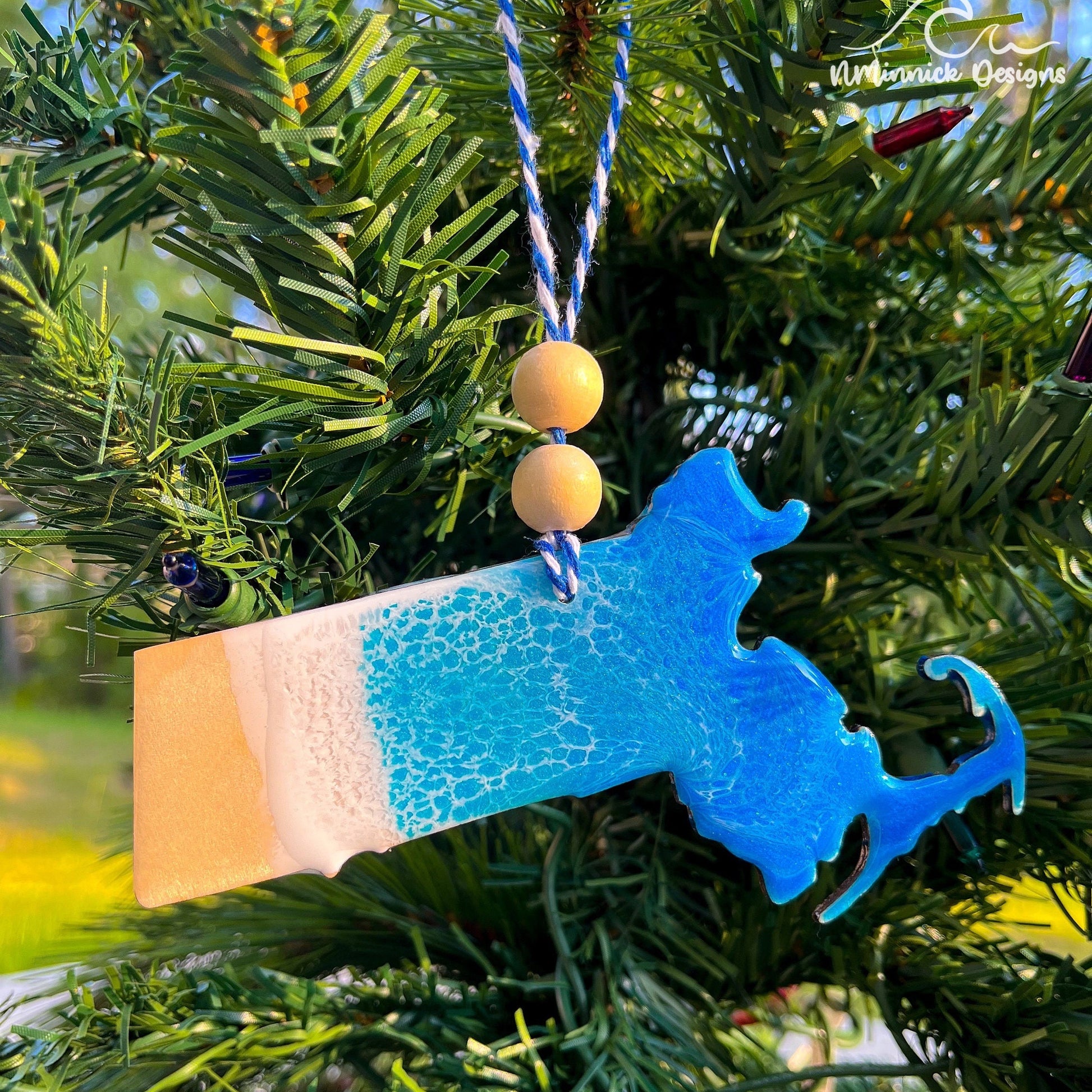 Massachusetts-shaped wooden Christmas ornament covered in blue and teal colored ocean resin art resembling the waves along Massachusetts&#39; Atlantic Coast. Finished with blue and white baker&#39;s twine and two wooden beads.