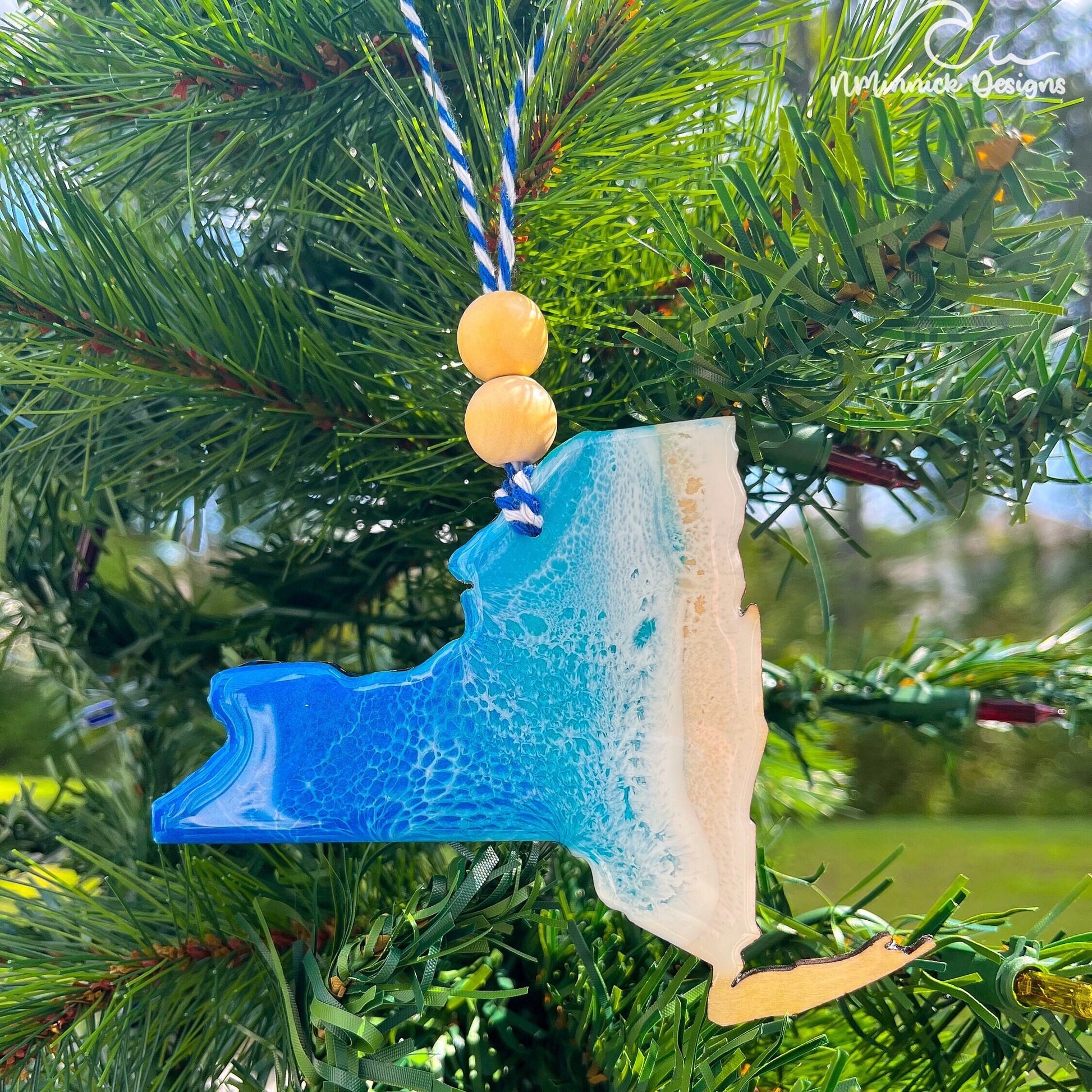 a new-york state shaped wooden christmas ornament covered in ocean blue and okinawa blue ocean resin art resembling ocean waves. Finished with baker&#39;s twine and two wooden beads and hanging on a tree.