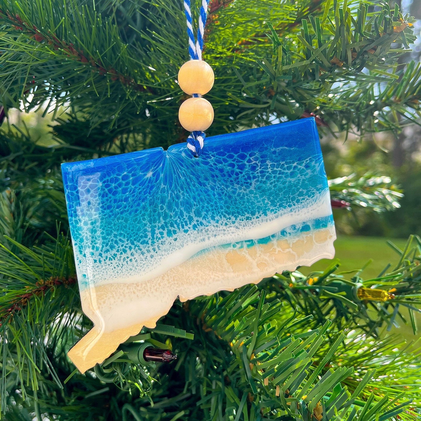 Connecticut Ornament with blue and white ocean resin art hanging on a christmas tree.