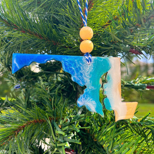 A Maryland shaped wooden Christmas ornament covered in blue ocean resin art, resembling the waves of the ocean. Finished with baker&#39;s twine and two wooden beads and hanging on a Christmas tree.