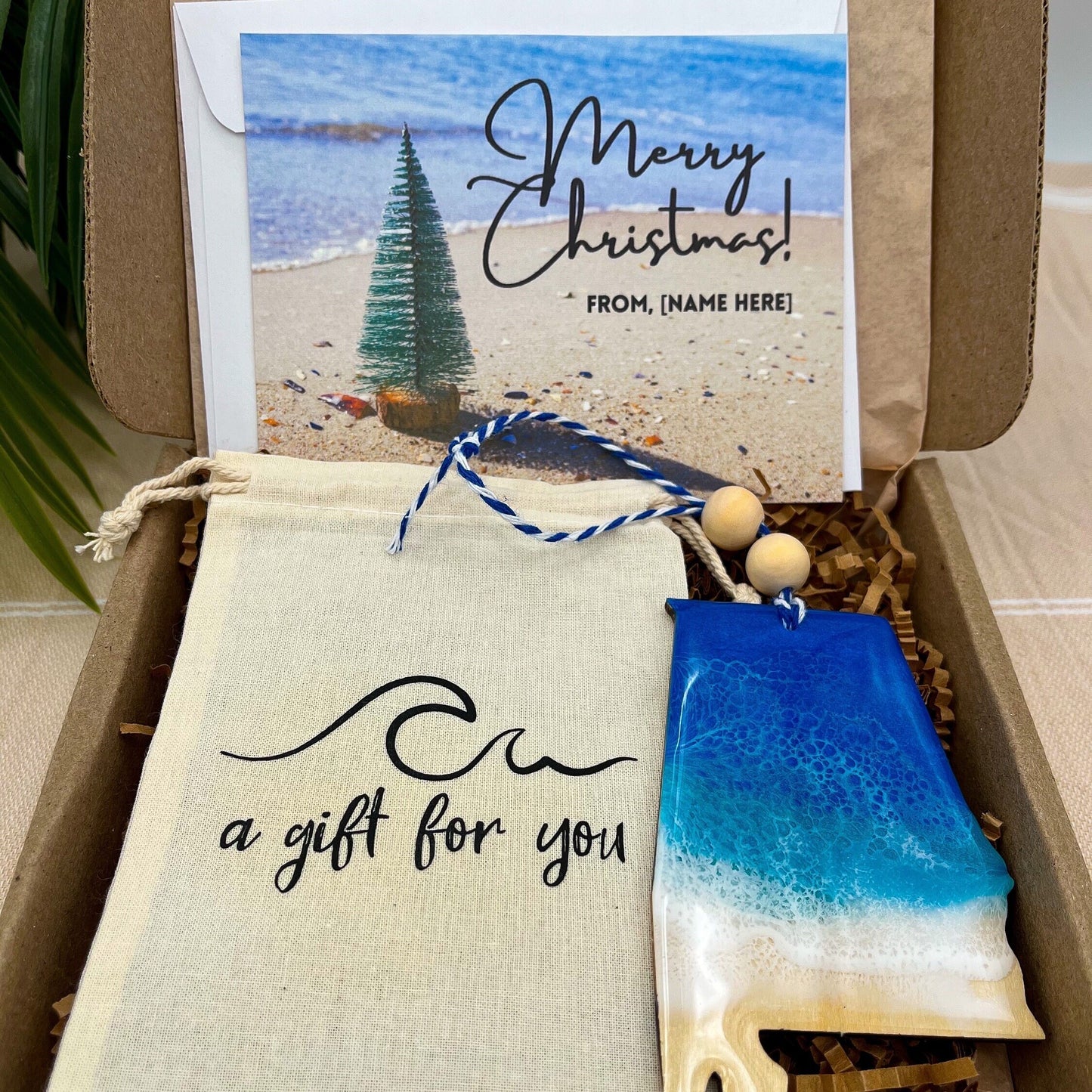 An Alabama shaped wooden christmas ornament with ocean resin art, resembling the waves of the ocean. In a box with an ornament keepsake bag with a wave that says &quot;a gift for you&quot; and a Merry Christmas custom card.