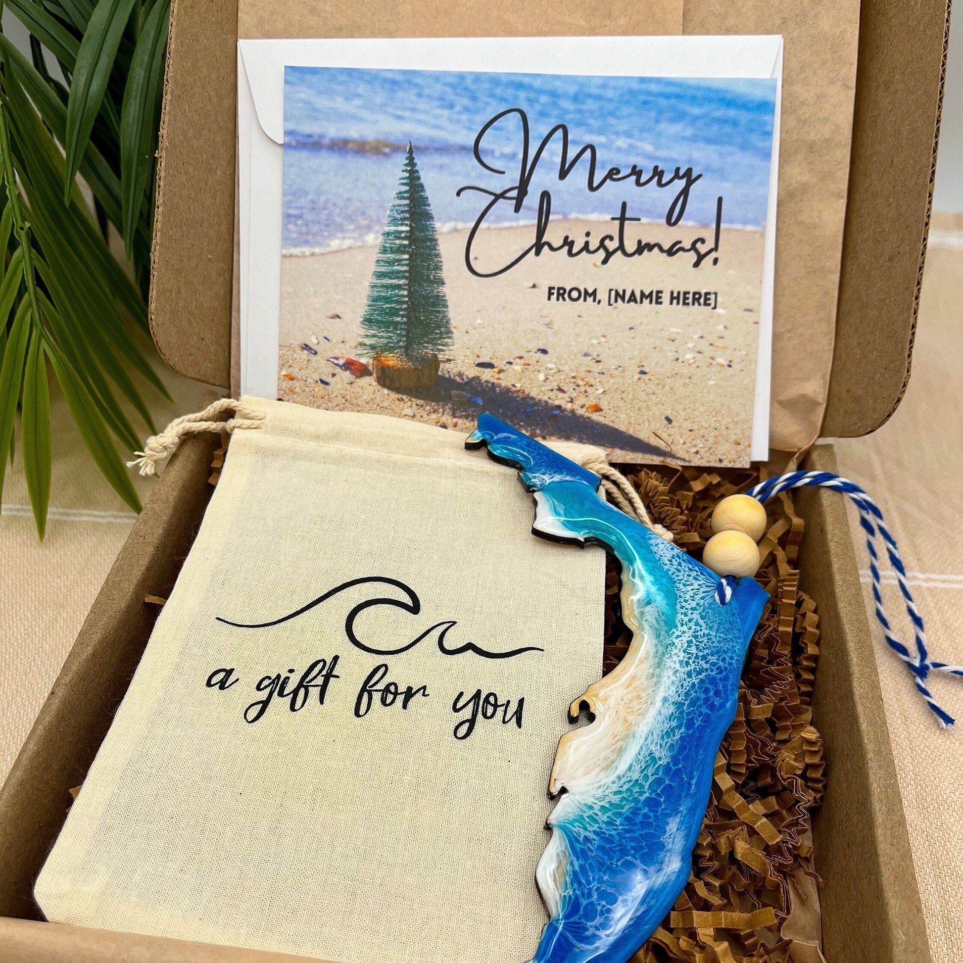 A Florida shaped wooden christmas ornament with ocean resin art, resembling the waves of the ocean. In a box with an ornament keepsake bag with a wave that says &quot;a gift for you&quot; and a Merry Christmas custom card.