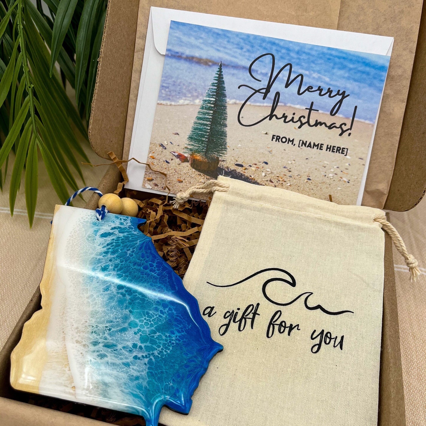 A Georgia shaped wooden christmas ornament with ocean resin art, resembling the waves of the ocean. In a box with an ornament keepsake bag with a wave that says &quot;a gift for you&quot; and a Merry Christmas custom card.