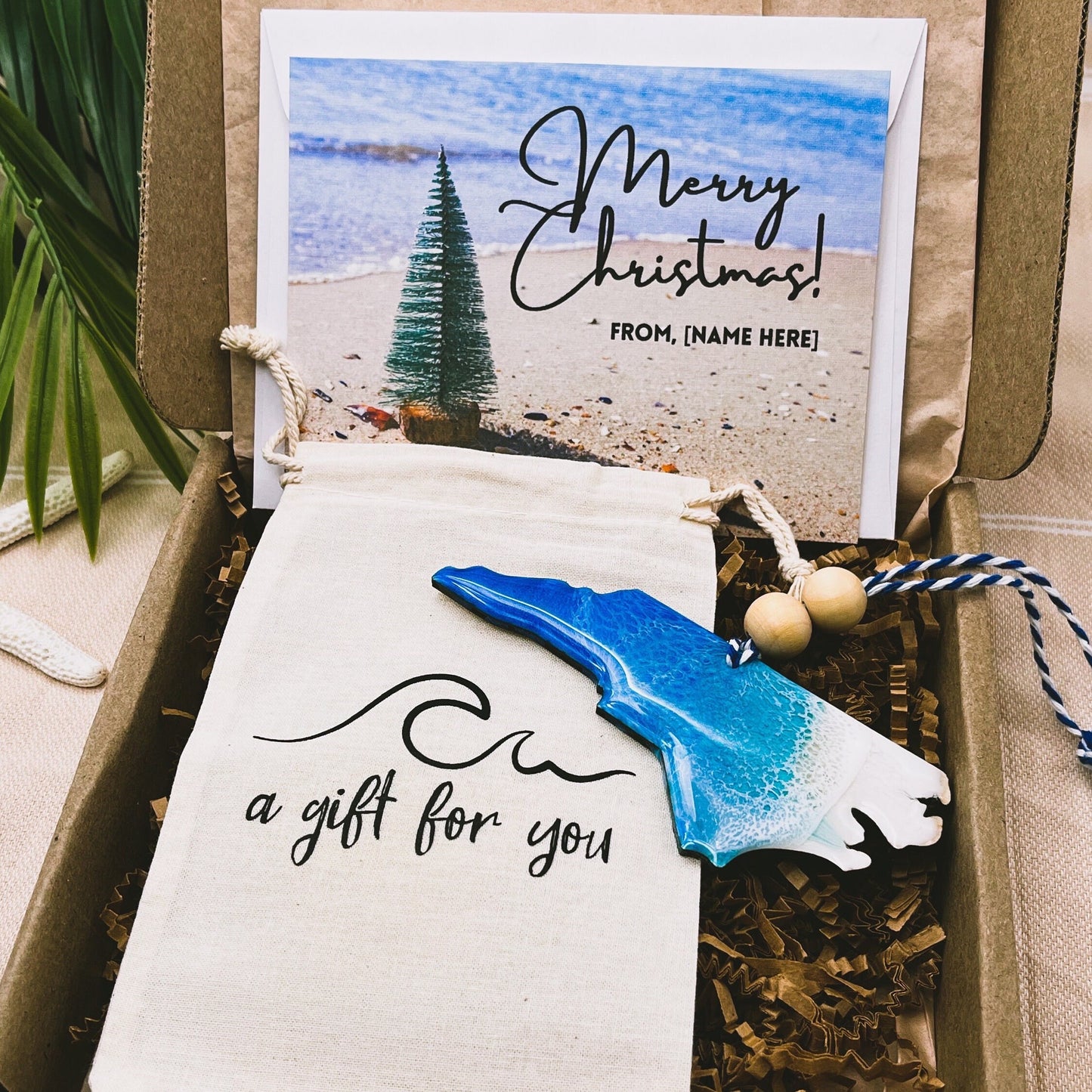 A North Carolina shaped wooden christmas ornament with ocean resin art, resembling the waves of the ocean. In a box with an ornament keepsake bag with a wave that says &quot;a gift for you&quot; and a Merry Christmas custom card.