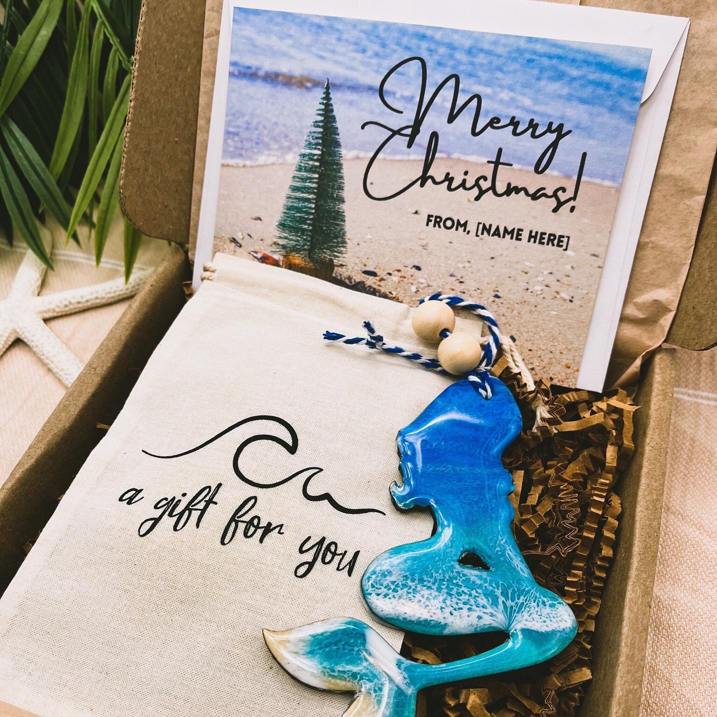 A Mermaid shaped wooden christmas ornament with ocean resin art, resembling the waves of the ocean. In a box with an ornament keepsake bag with a wave that says &quot;a gift for you&quot; and a Merry Christmas custom card.