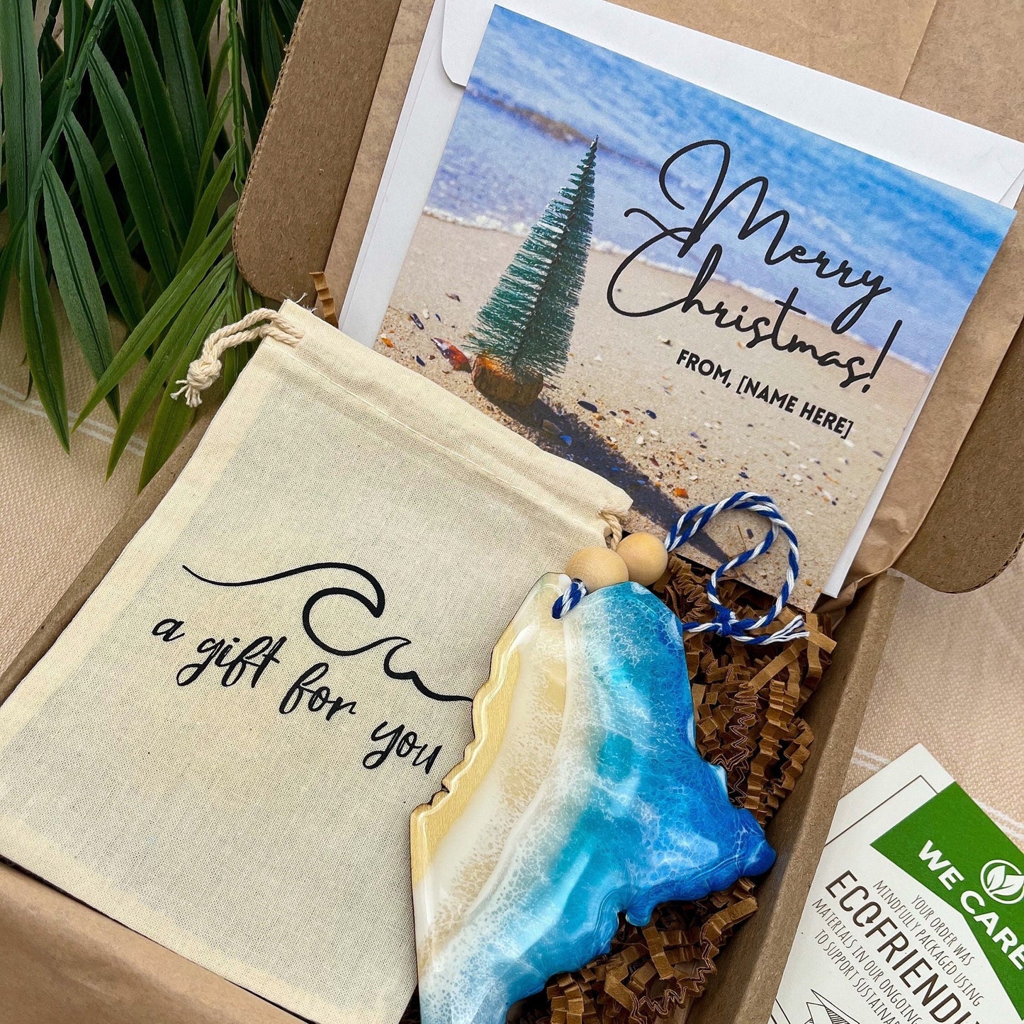 A Maine shaped wooden christmas ornament with ocean resin art, resembling the waves of the ocean. In a box with an ornament keepsake bag with a wave that says &quot;a gift for you&quot; and a Merry Christmas custom card.