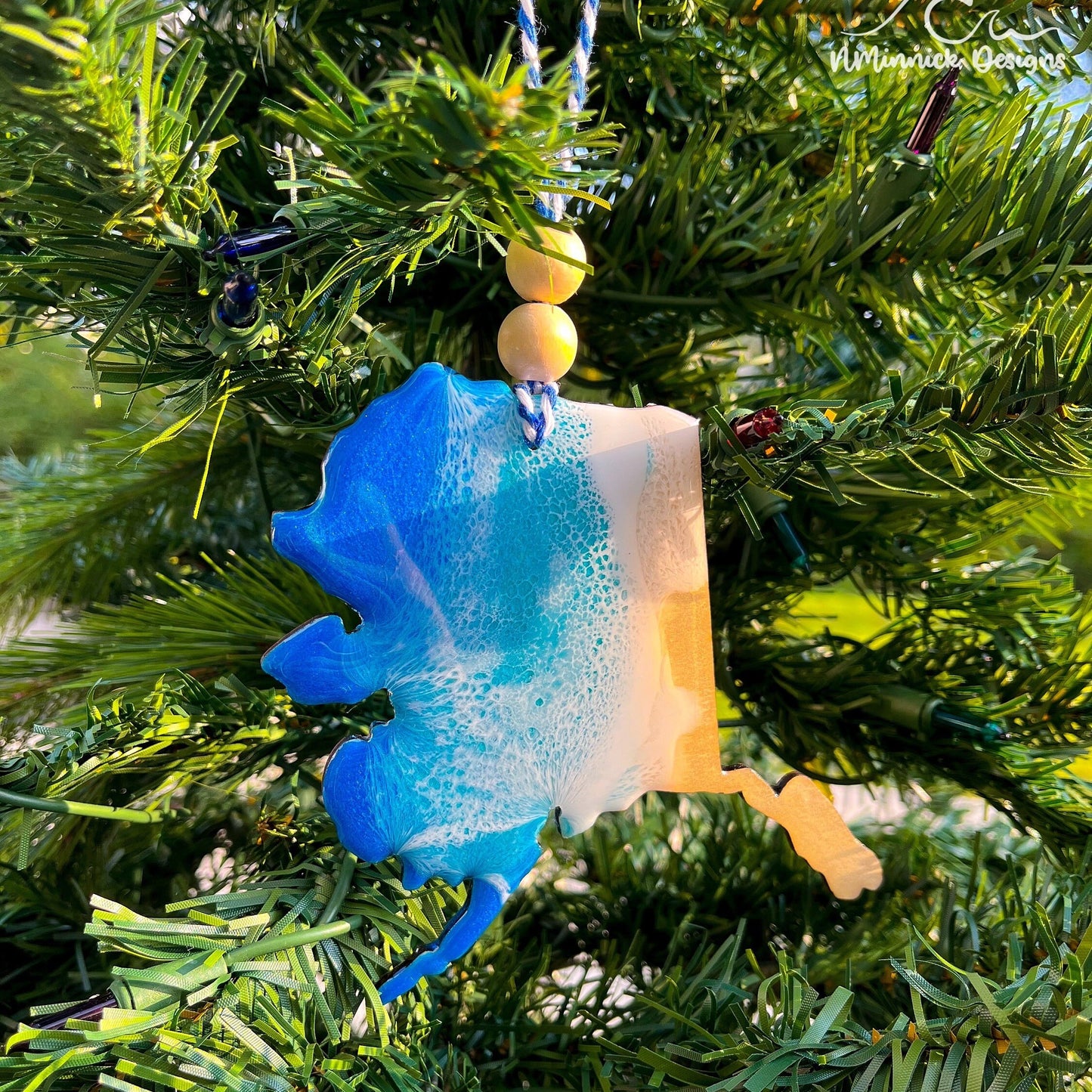 Alaska-shaped wooden Christmas ornament covered in blue and teal colored ocean resin art resembling the waves along Alaska&#39;s Pacific Coast. Finished with blue and white baker&#39;s twine and two wooden beads.
