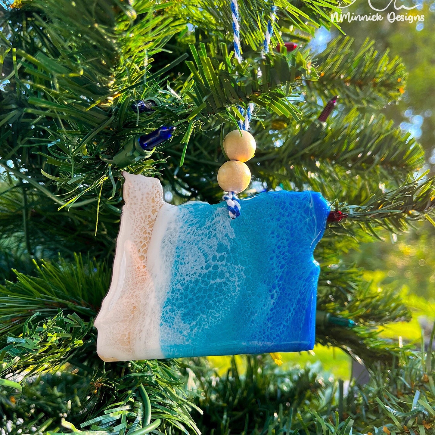 Oregon-shaped wooden Christmas ornament covered in blue and teal colored ocean resin art resembling the waves along Oregon&#39;s Pacific Coast. Finished with blue and white baker&#39;s twine and two wooden beads.