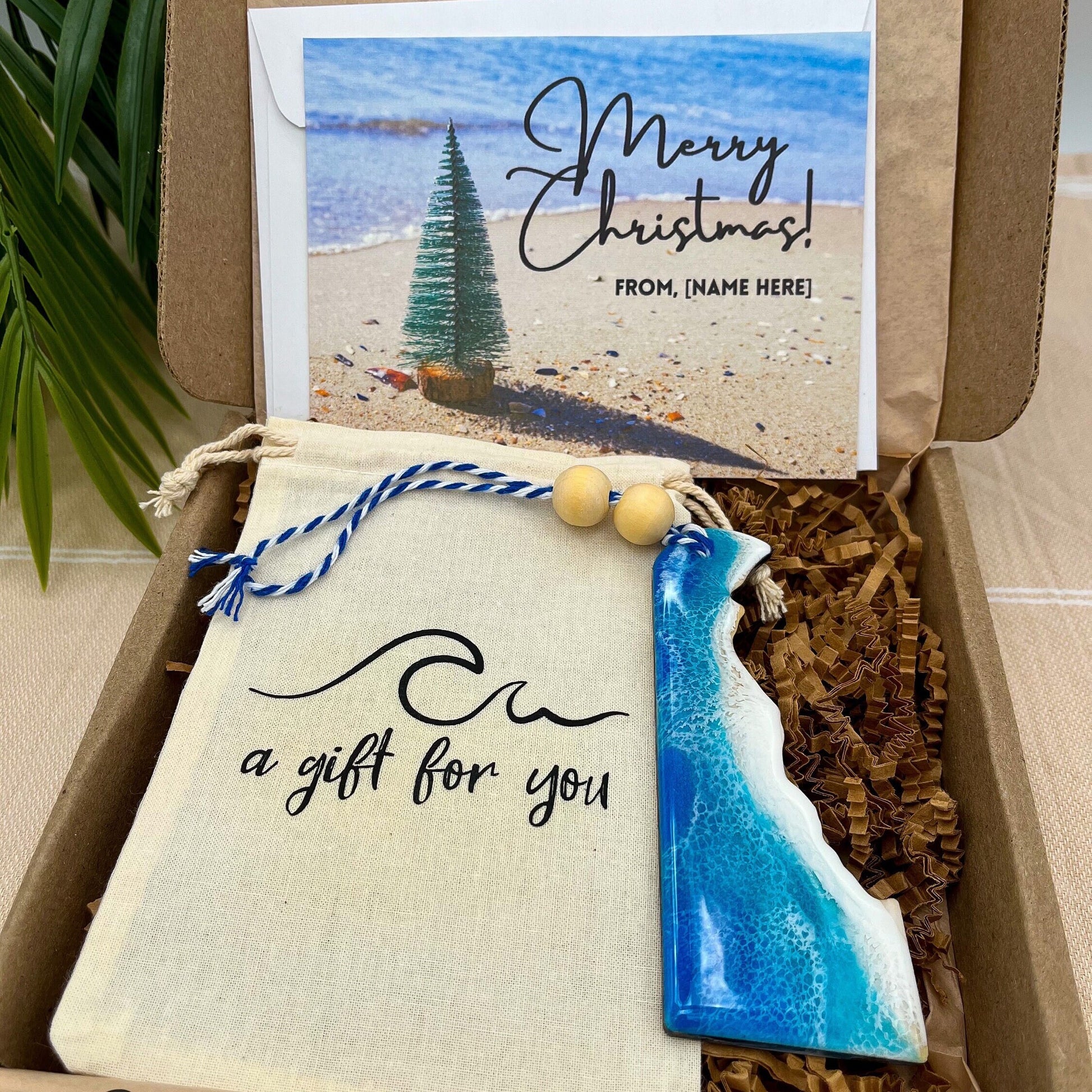 A Delaware shaped wooden christmas ornament with ocean resin art, resembling the waves of the ocean. In a box with an ornament keepsake bag with a wave that says &quot;a gift for you&quot; and a Merry Christmas custom card.