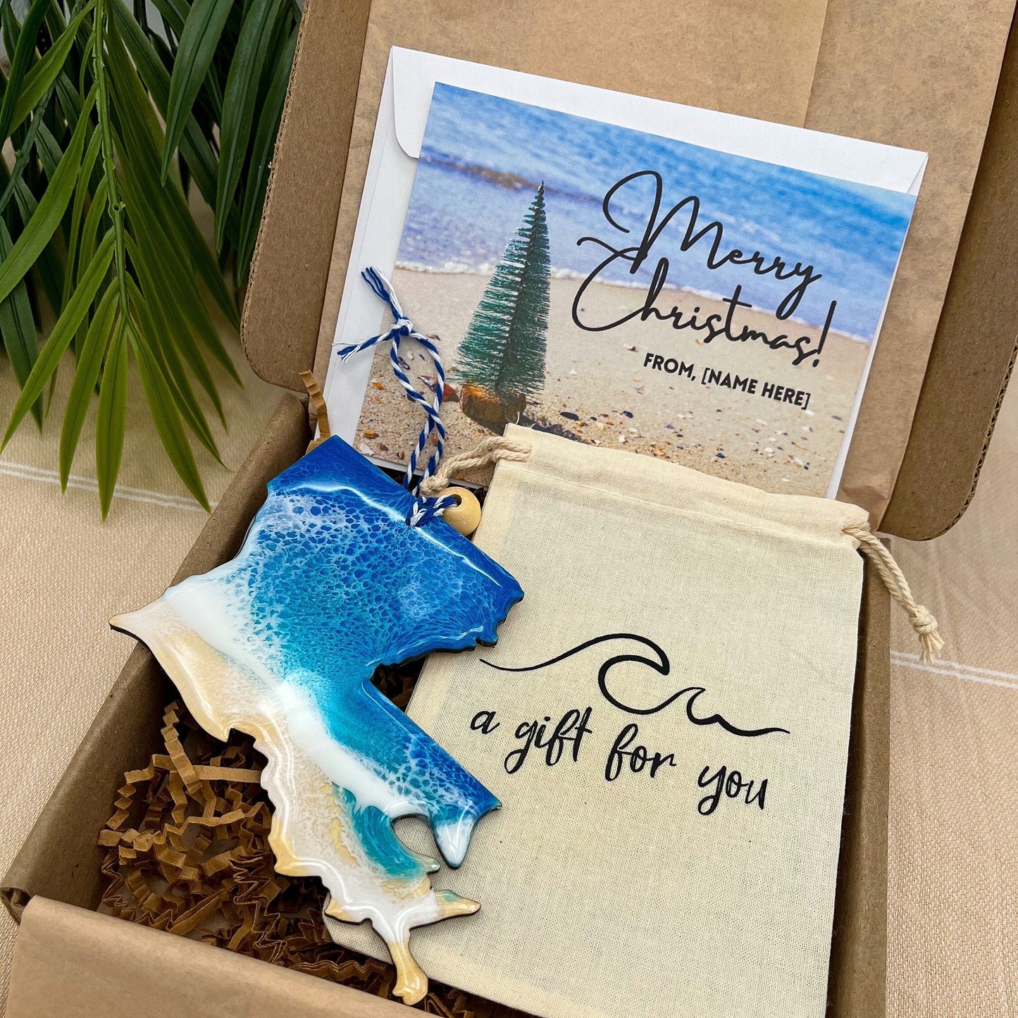 A Louisiana shaped wooden christmas ornament with ocean resin art, resembling the waves of the ocean. In a box with an ornament keepsake bag with a wave that says &quot;a gift for you&quot; and a Merry Christmas custom card.