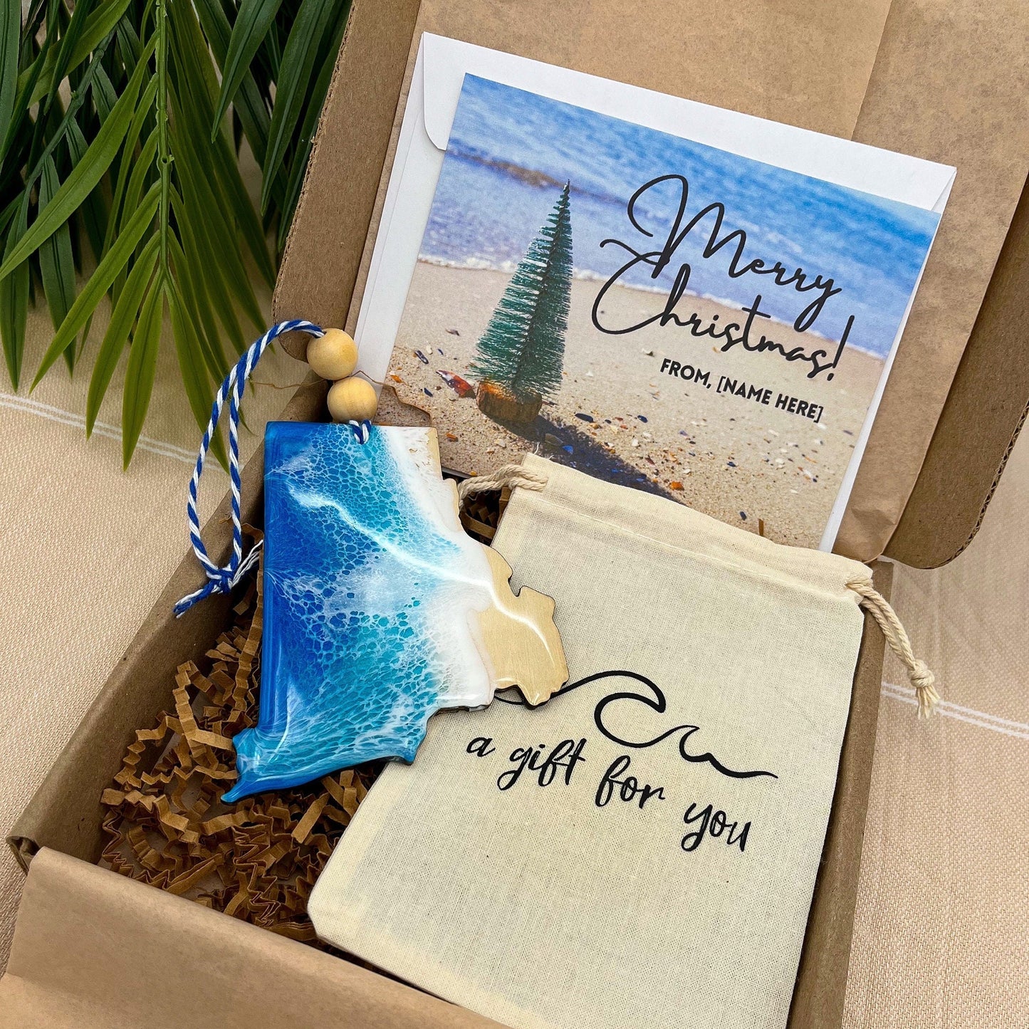 A Rhode Island shaped wooden christmas ornament with ocean resin art, resembling the waves of the ocean. In a box with an ornament keepsake bag with a wave that says &quot;a gift for you&quot; and a Merry Christmas custom card.