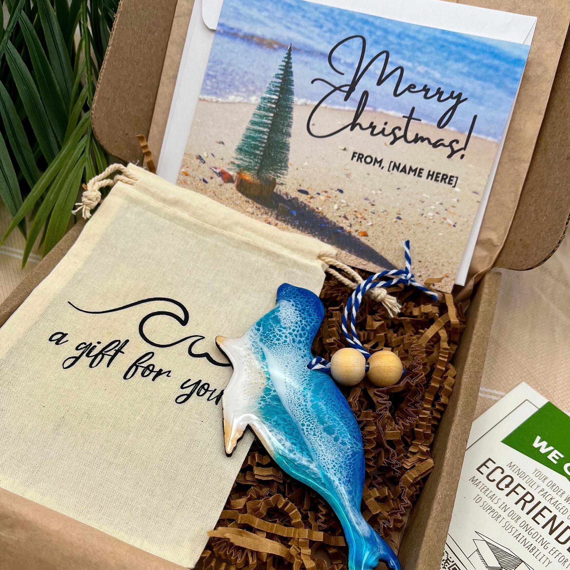 A seal shaped wooden christmas ornament with ocean resin art, resembling the waves of the ocean. In a box with an ornament keepsake bag with a wave that says &quot;a gift for you&quot; and a Merry Christmas custom card.