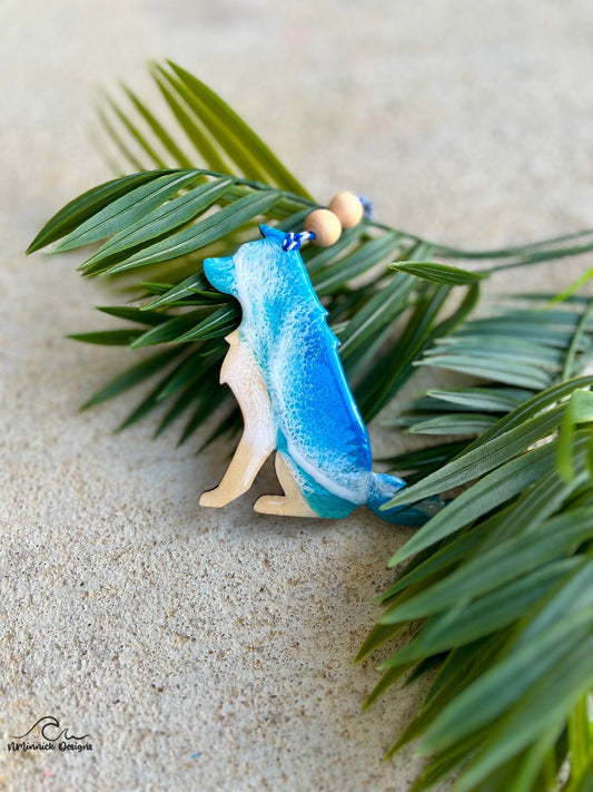 Dog shaped ornament with ocean resin art laying against palm leaves.