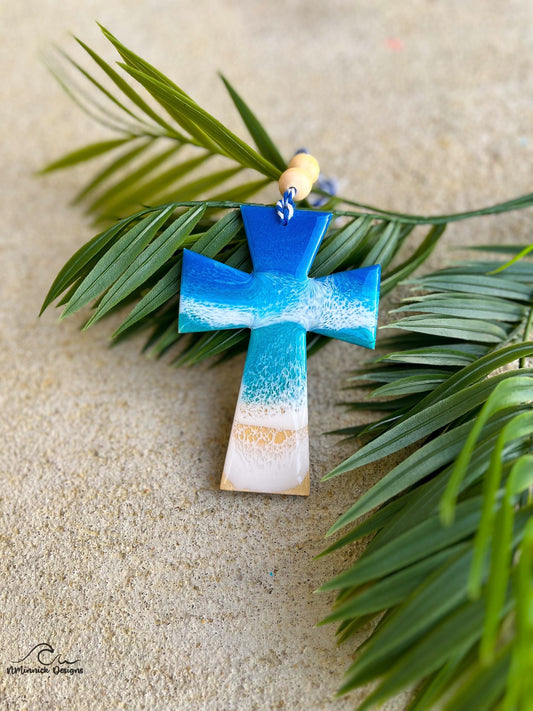 Cross ornament with ocean resin art laying against palm leaves.