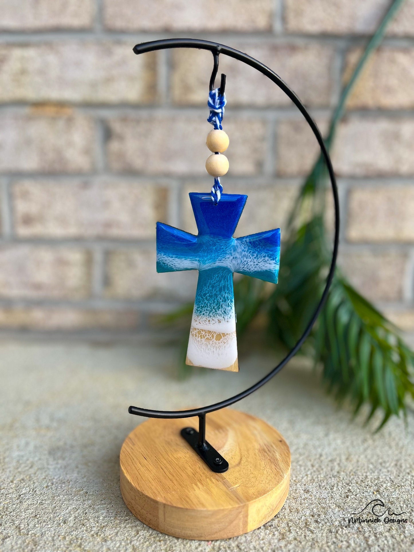 Cross shaped ornament with ocean resin art and hanging from an ornament stand.