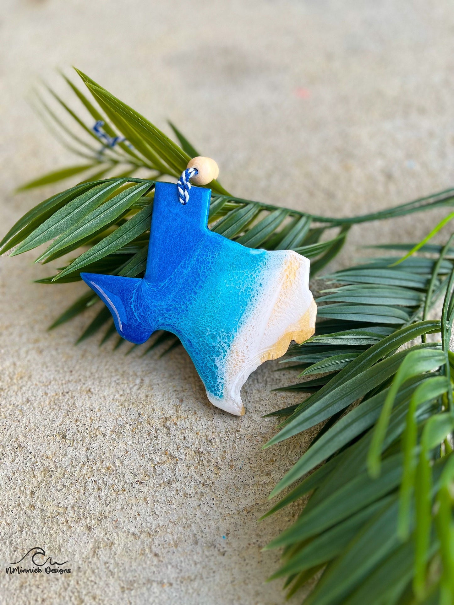 Texas ornament with ocean resin art laying against palm leaves.