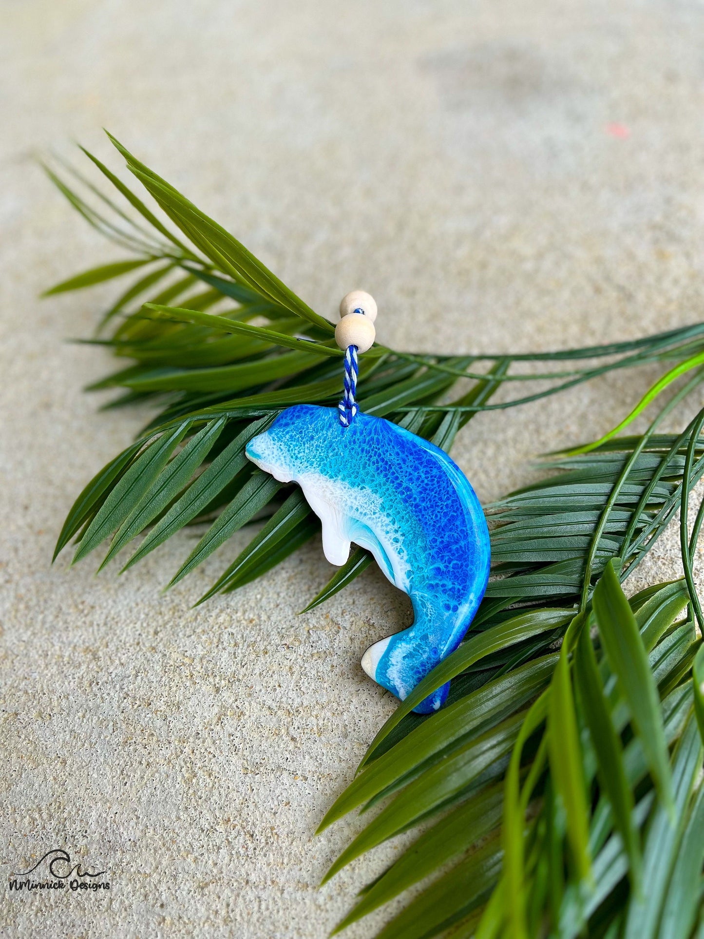 Manatee shaped ornament with ocean resin art laying against palm leaves.