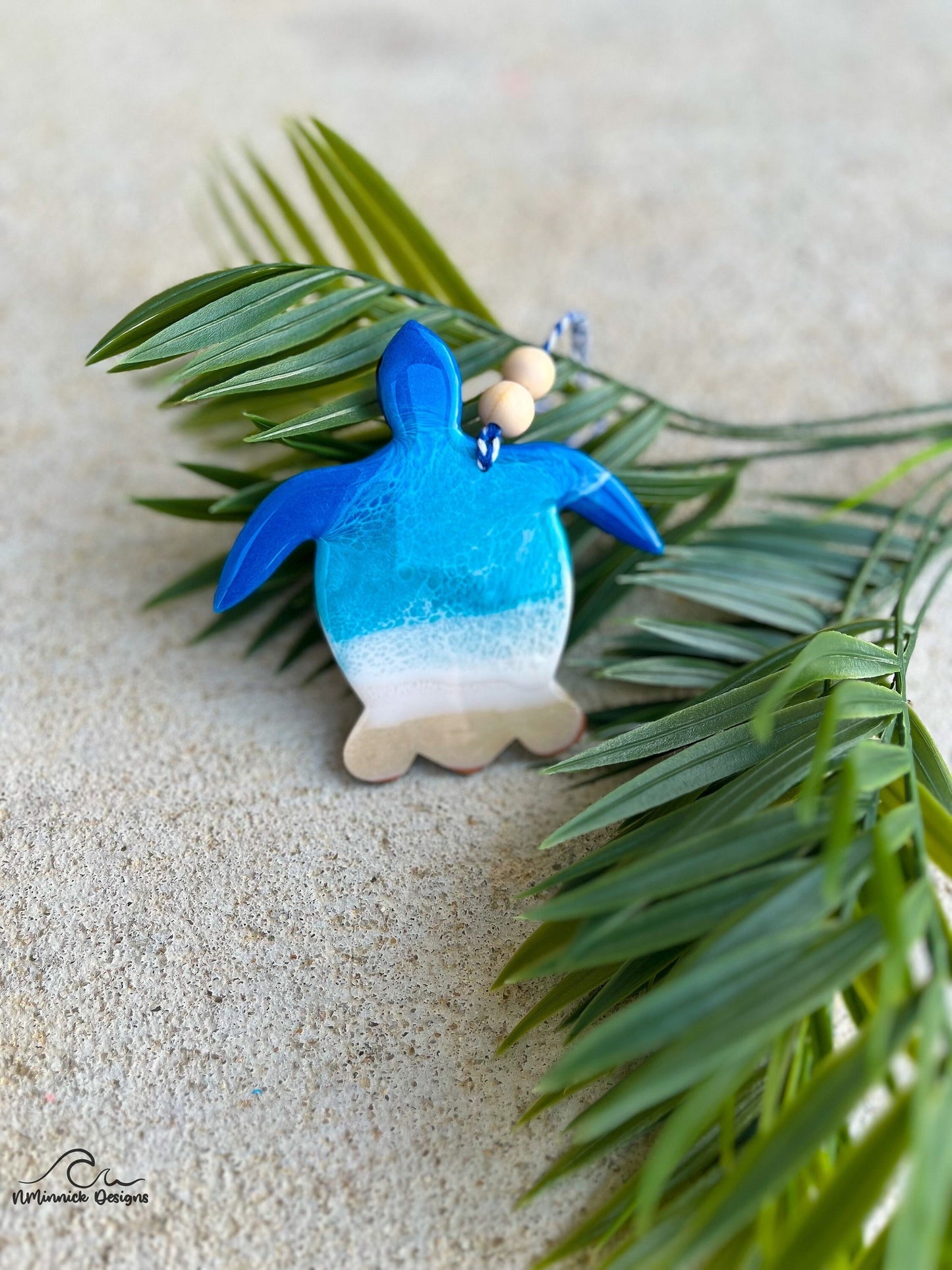 Sea Turtle Ornament with ocean wave art laying against palm leaves.
