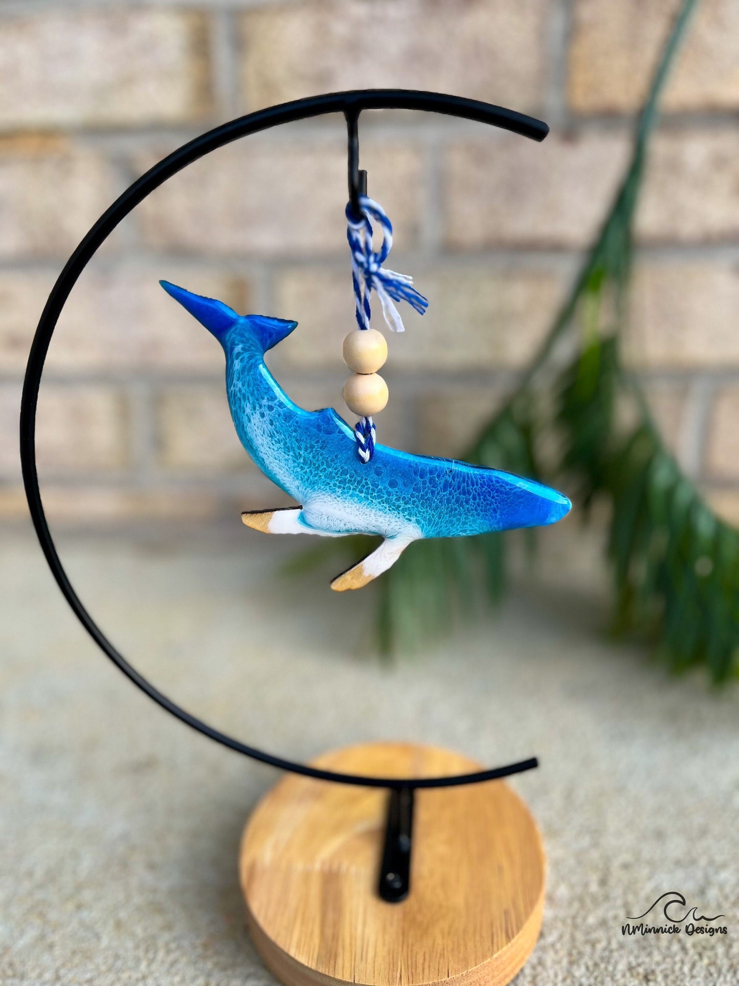 A humpback whale shaped ornament with blue and white ocean resin art, hanging on an ornament stand.