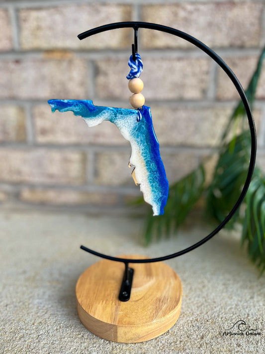 A florida shaped wooden ornament with blue and white ocean resin art. Finished with two wooden beads and a stand of bakers twine.