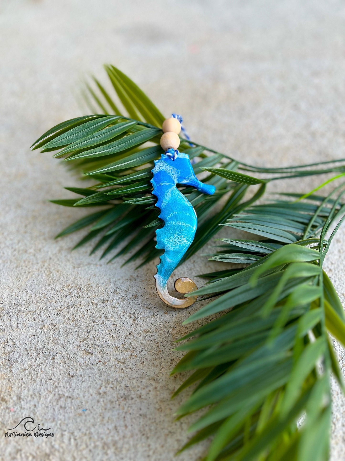 Seahorse ornament with ocean resin art laying against palm leaves