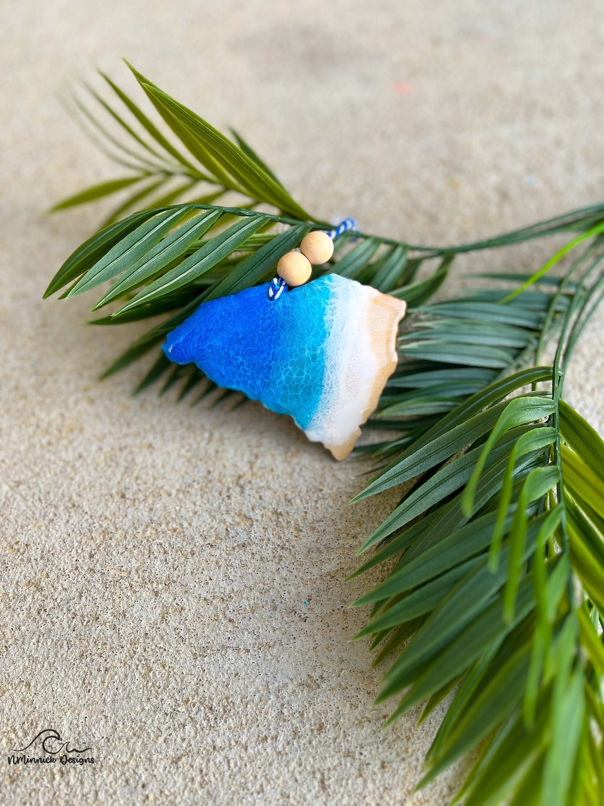 South Carolina shaped ornament with ocean resin art laying against palm leaves.