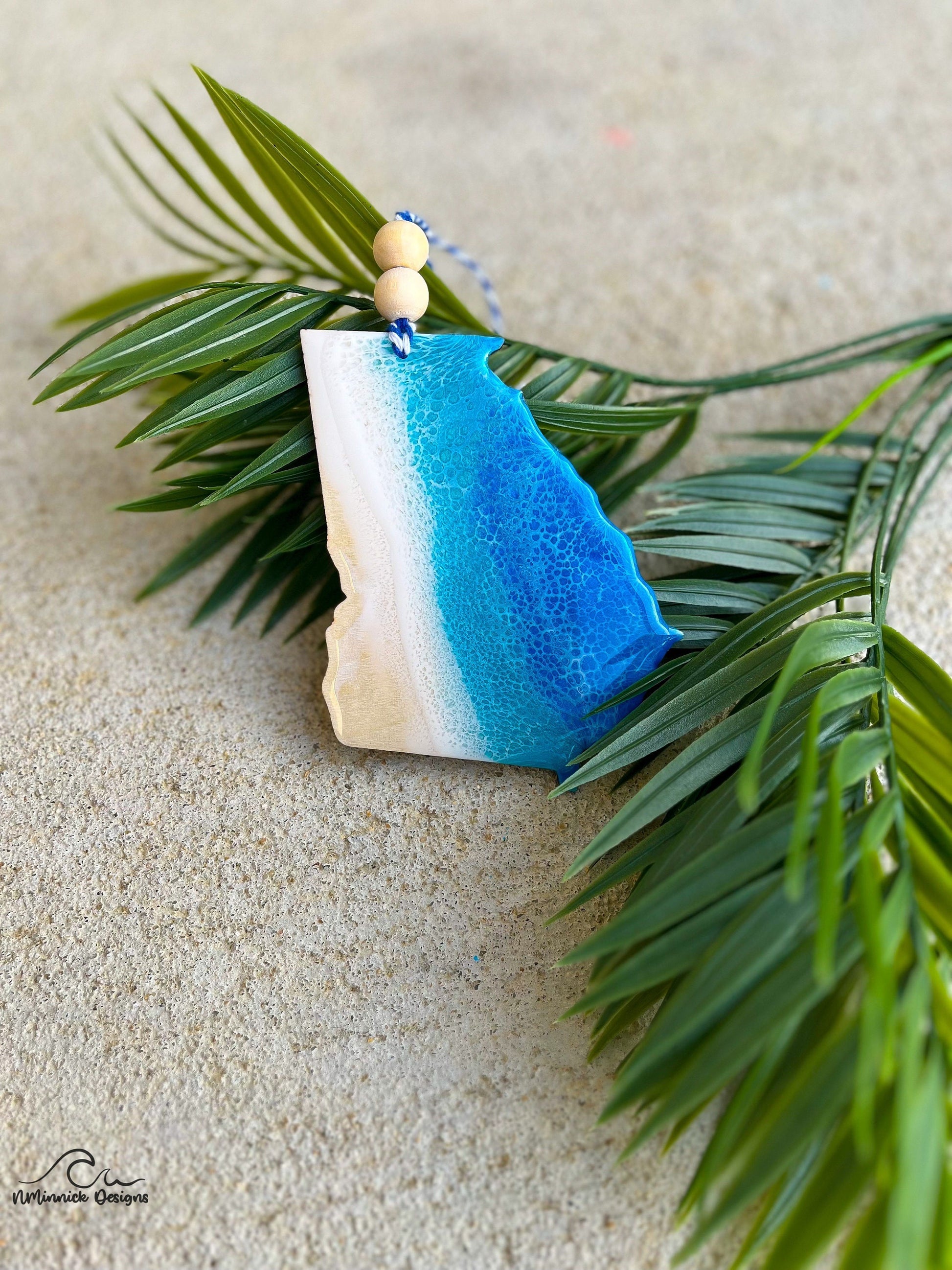 Georgia ornament with ocean resin art laying against palm leaves