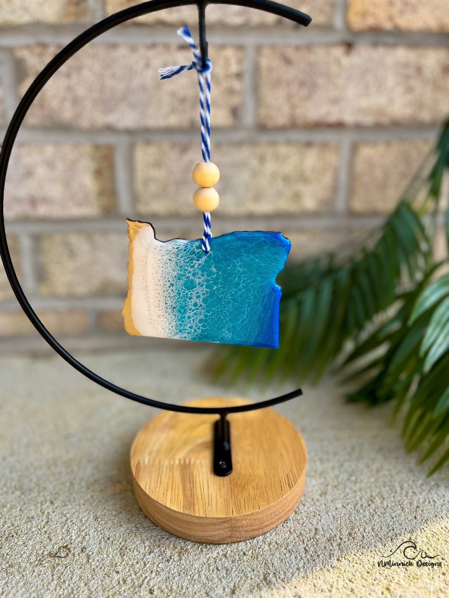 Oregon shaped ornament with ocean resin art along the coast and hanging from an ornament stand.