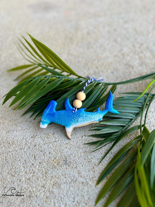 Hammerhead Shark ornament with ocean resin art laying against palm leaves.