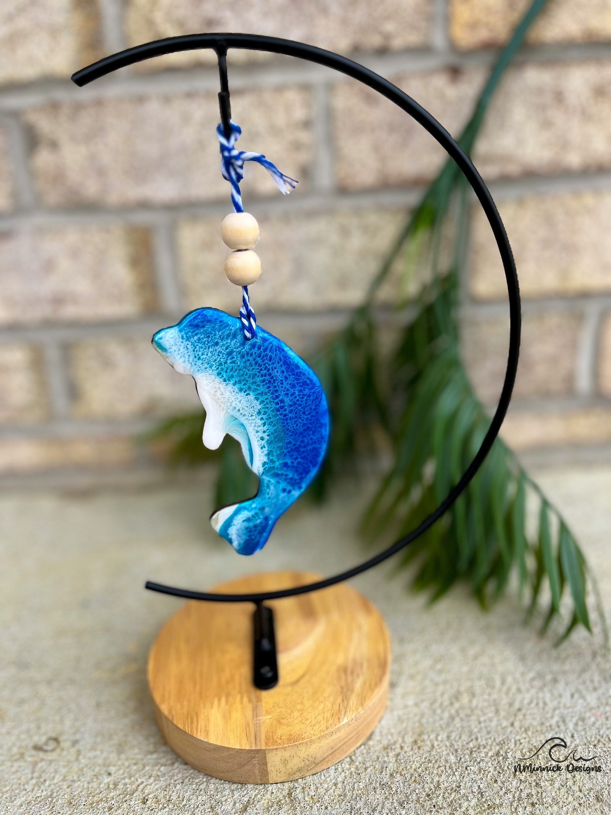 Manatee shaped ocean resin ornament with two wooden beads and hanging from an ornament stand.
