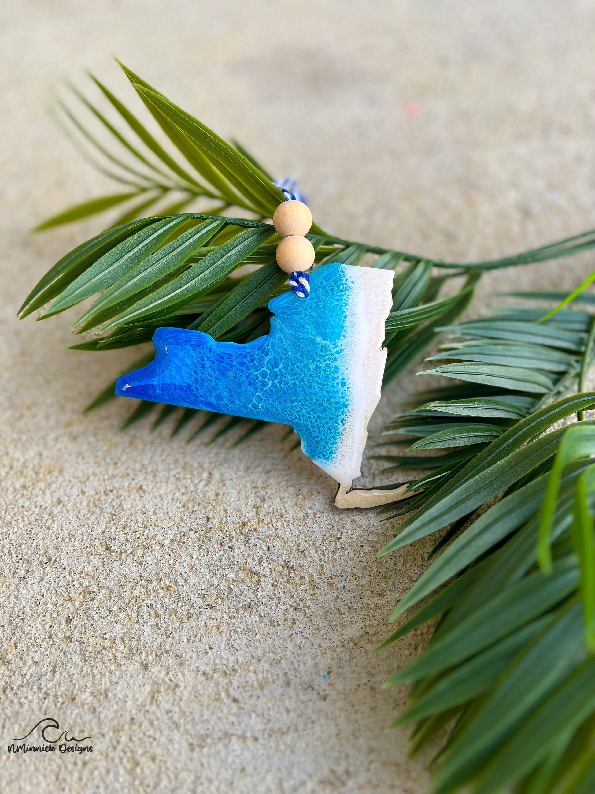 New York ornament with ocean resin art laying against palm leaves.