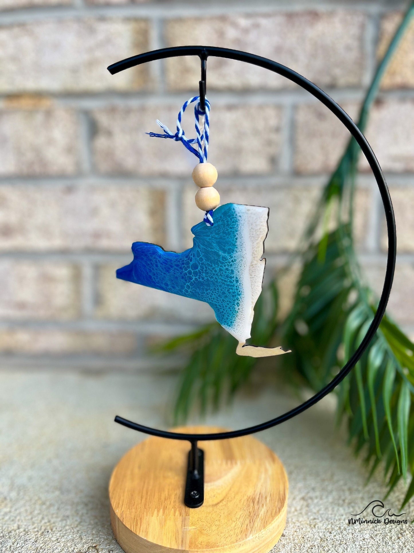 New York beach ornament with ocean wave art hanging from an ornament stand.