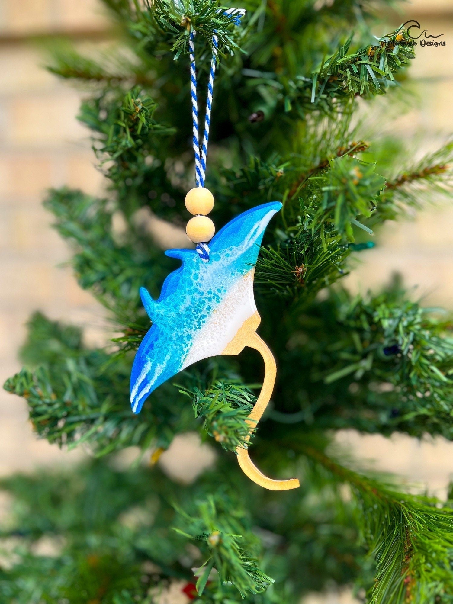 Manta Ray shaped wooden ornament with one side coated in blue ocean resin wave art and hanging on a christmas tree.