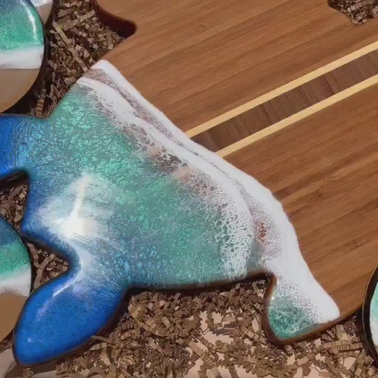 Sea turtle-shaped bamboo board covered in aoi hi blue and okinawa green ocean resin art to resemble the waves of the ocean.  Matching set of 4 round drink coasters also with blue and green ocean resin art and cork backings.  Laying in an eco-friendly and plastic-free gift box.